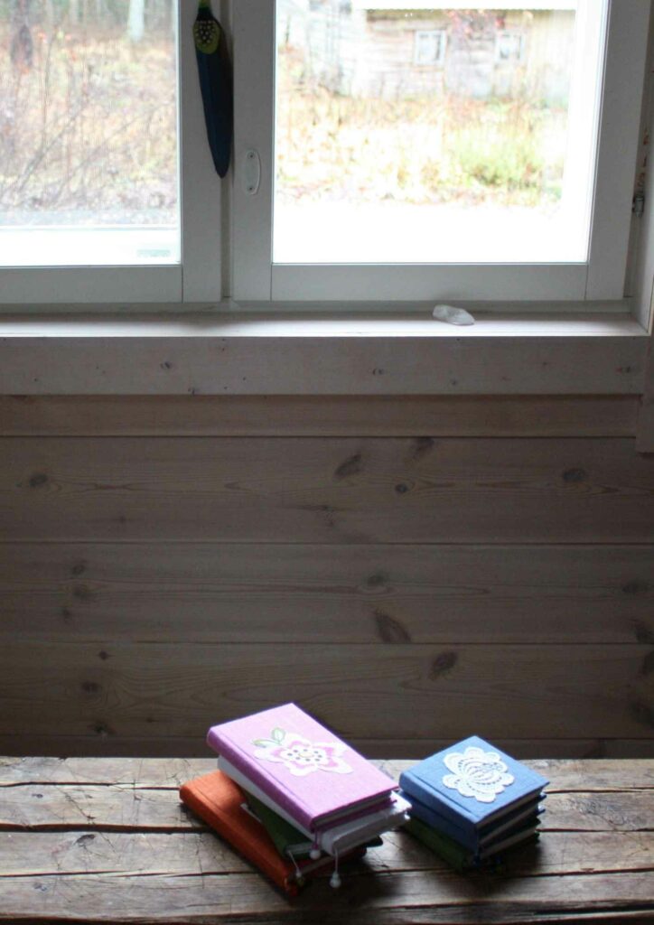 TuuliHelmen käsintehtyjen kirjojen kuvausta tuvan penkillä ikkunan edessä